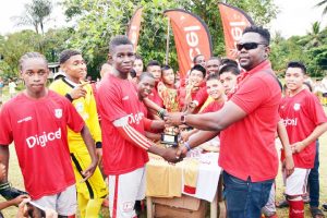 Digicel representative Shawn Weatherspoon hands over the winning trophy and new uniforms to Captain of Mahdia Secondary Travis  following the completion of the final on Saturday.