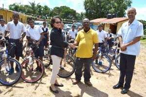 First Lady, Mrs. Sandra Granger and Mahdia businessman, Mr. Roger Hinds shake hands as Regional Executive Officer, Mr. Rafel Downes and some of the recipients of spanking new bikes look on. 