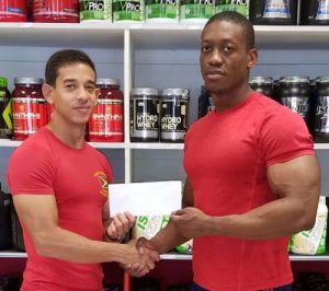 Fitness Express Manager Jamie Mc Donald (left) hands over the air ticket to Mr. Guyana Kerwyn Clarke. 