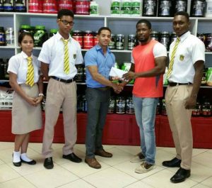 Phys Ed. Teacher Mr. Jaryl Moore (right) accepts the donation from Fitness Express’ Jamie McDonald while members of the fifth form Physical Education class looks on.