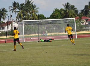 T&T’s Under-20 Captain, Jabari Mitchell (not pictured) nets their opening goal against Alpha United’s goalie, Alex Murray. (Franklin Wilson photo)