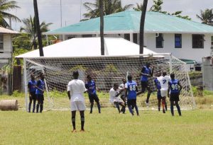 This Buxton United (Blue) heads the ball away and out of danger against Mahaica Determinators.