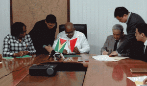 Minister of Finance Winston Jordan (centre) signs the framework agreement along with outgoing Chinese Ambassador to Guyana Zhang Limin (3rd from right).