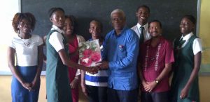 Joanna Archer (second, left) receives the gear from Gervy C. Harry while Headmaster of West Demerara Secondary, Harrinarine (second, right) among other teachers and students share the moment.