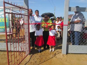 Minister Volda Lawerence assisted by two children cuts the ribbon to open the Play Park.