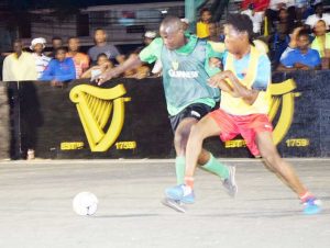 Players from North Ruimveldt (yellow bib) and West Back Road battle for possession of the ball during their encounter on Saturday night at Burnham Court. 