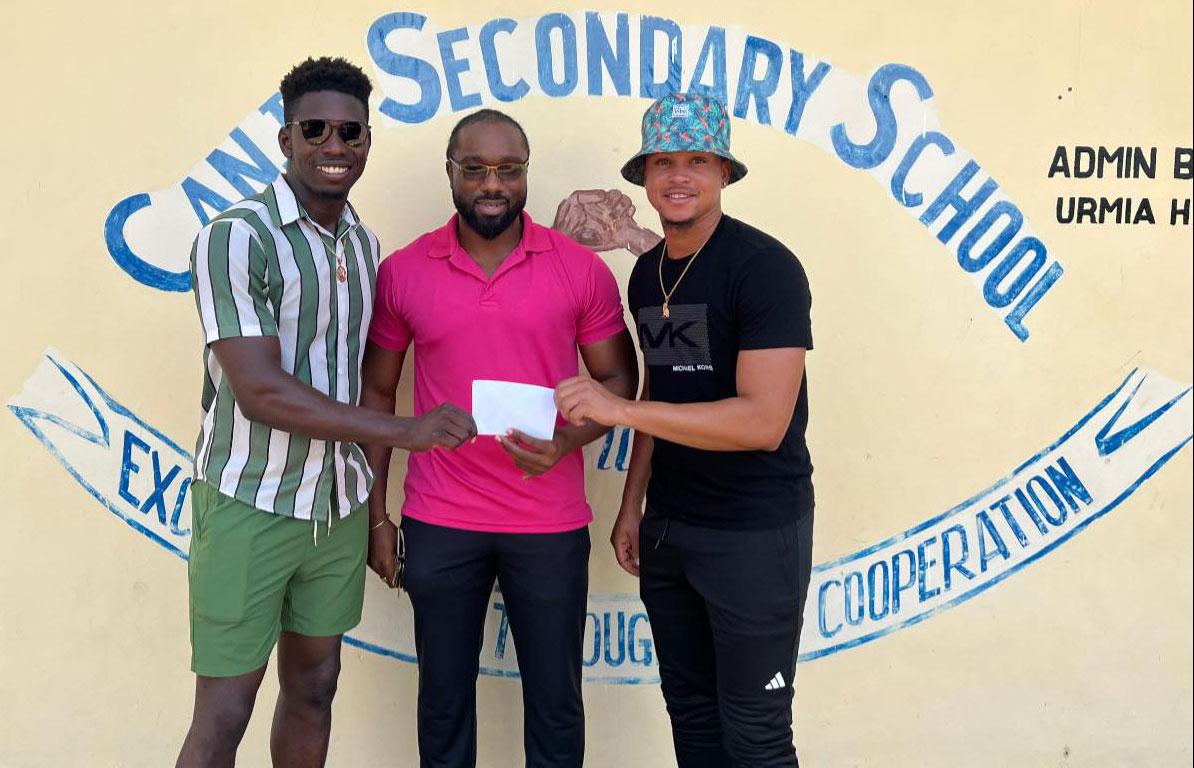West Indies All rounder Kevin Sinclair (left) and Guyana Fast Bowler Nial Smith (right) hand over their donation to a teacher of the school.